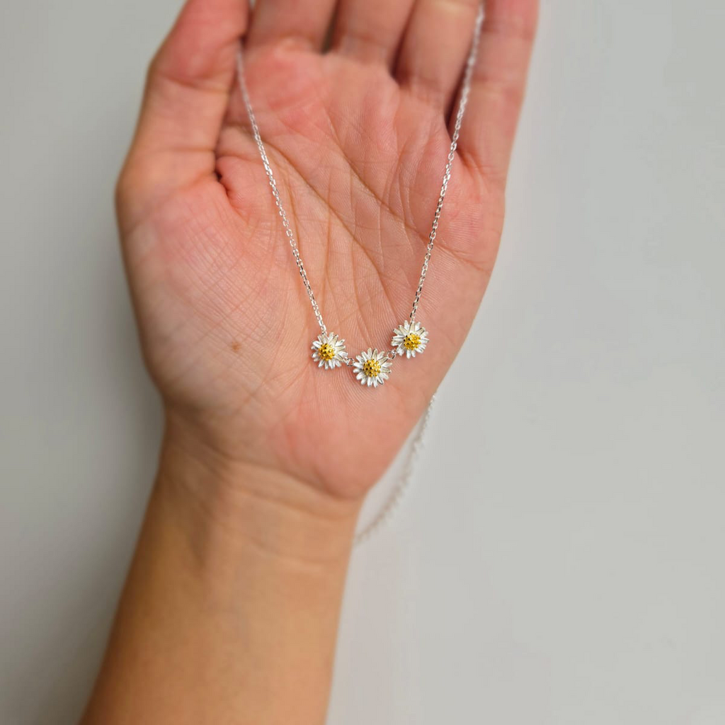A sterling silver necklace with three daisy details held in the palm of a hand.