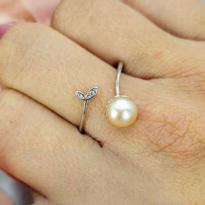An adjustable pearl ring with a leaf design on a person's hand.