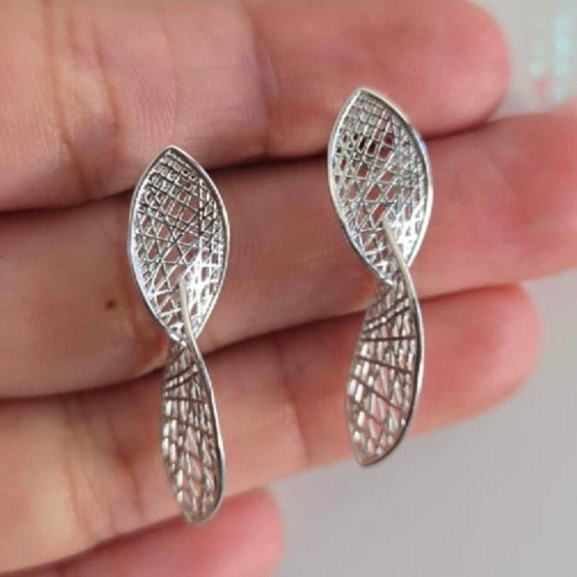 Silver earrings with intricate designs held between fingers against a neutral background