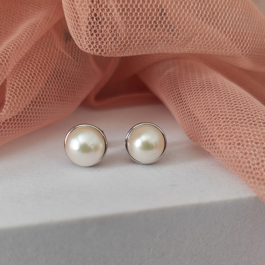 Pearl stud earrings on a light pink fabric background