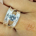A person's hand displaying a silver-colored ring with a large cubic zirconia stone set in a modern, elegant design.