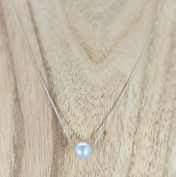 A sterling silver necklace with a single grey freshwater pearl presented on a wooden surface.