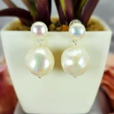 A pair of double drop freshwater pearl earrings displayed in a white container with a potted plant in the background.