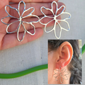 Silver flower-shaped earrings held in a hand with an inset showing them worn on an ear.
