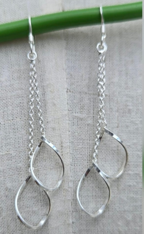 Silver teardrop earrings hanging from a green stick on a gray fabric background