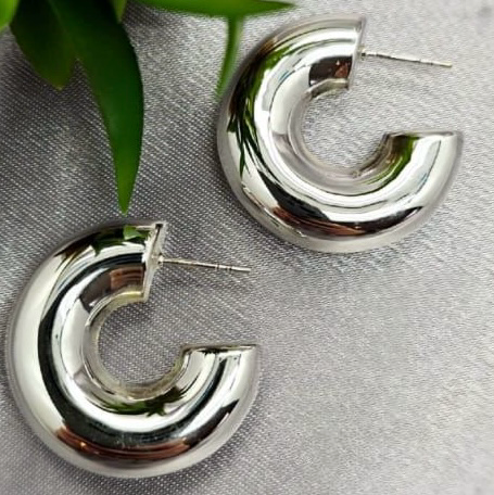 A pair of sterling silver hoop earrings displayed on a surface with a blurred green background.