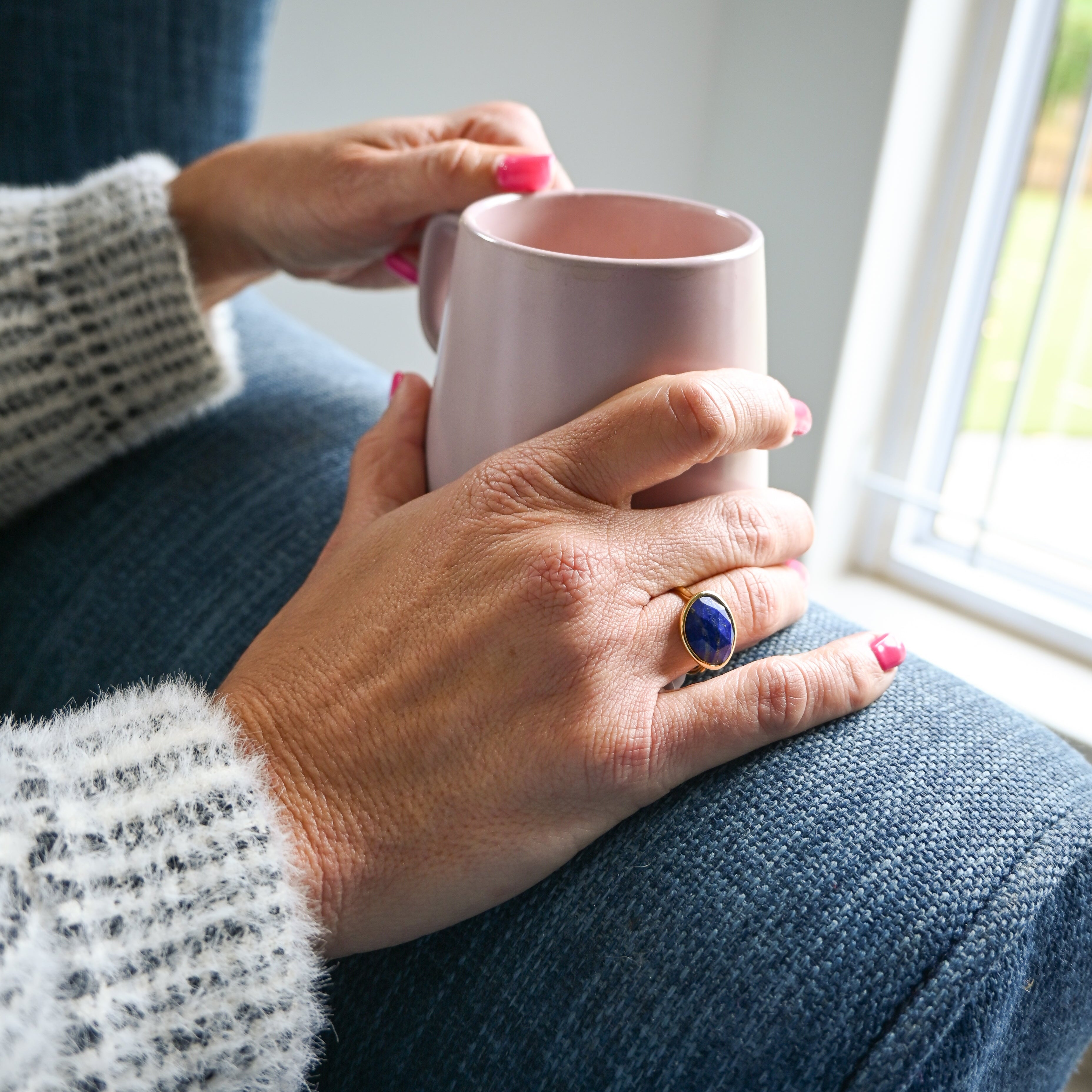 Person holding a pink mug with a ring on a blue cushioned chair.