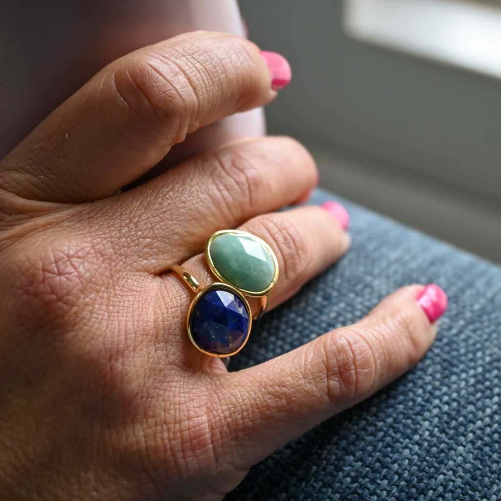 Hand wearing a ring with two gemstones on a neutral background