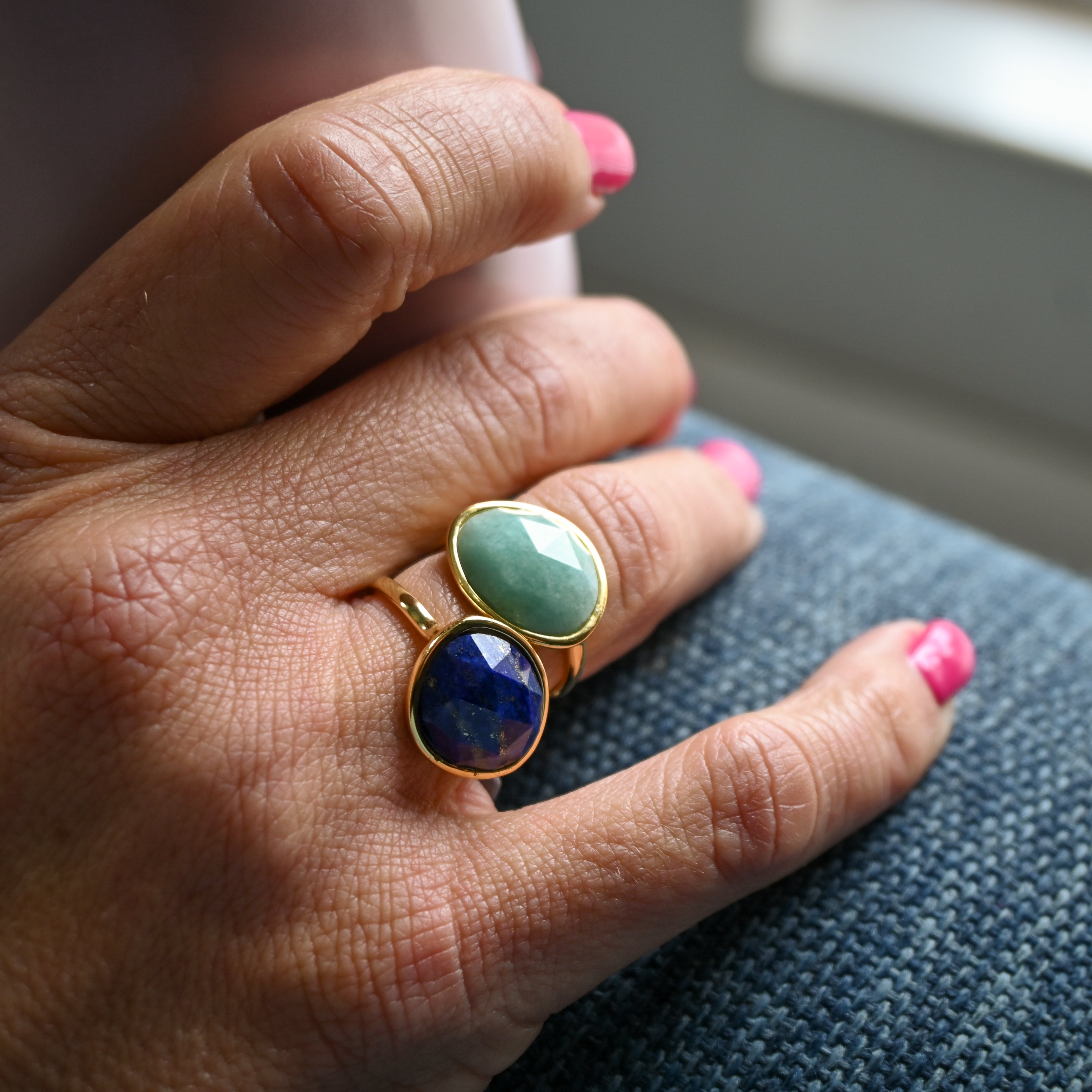 Hand wearing a ring with two gemstones on a neutral background
