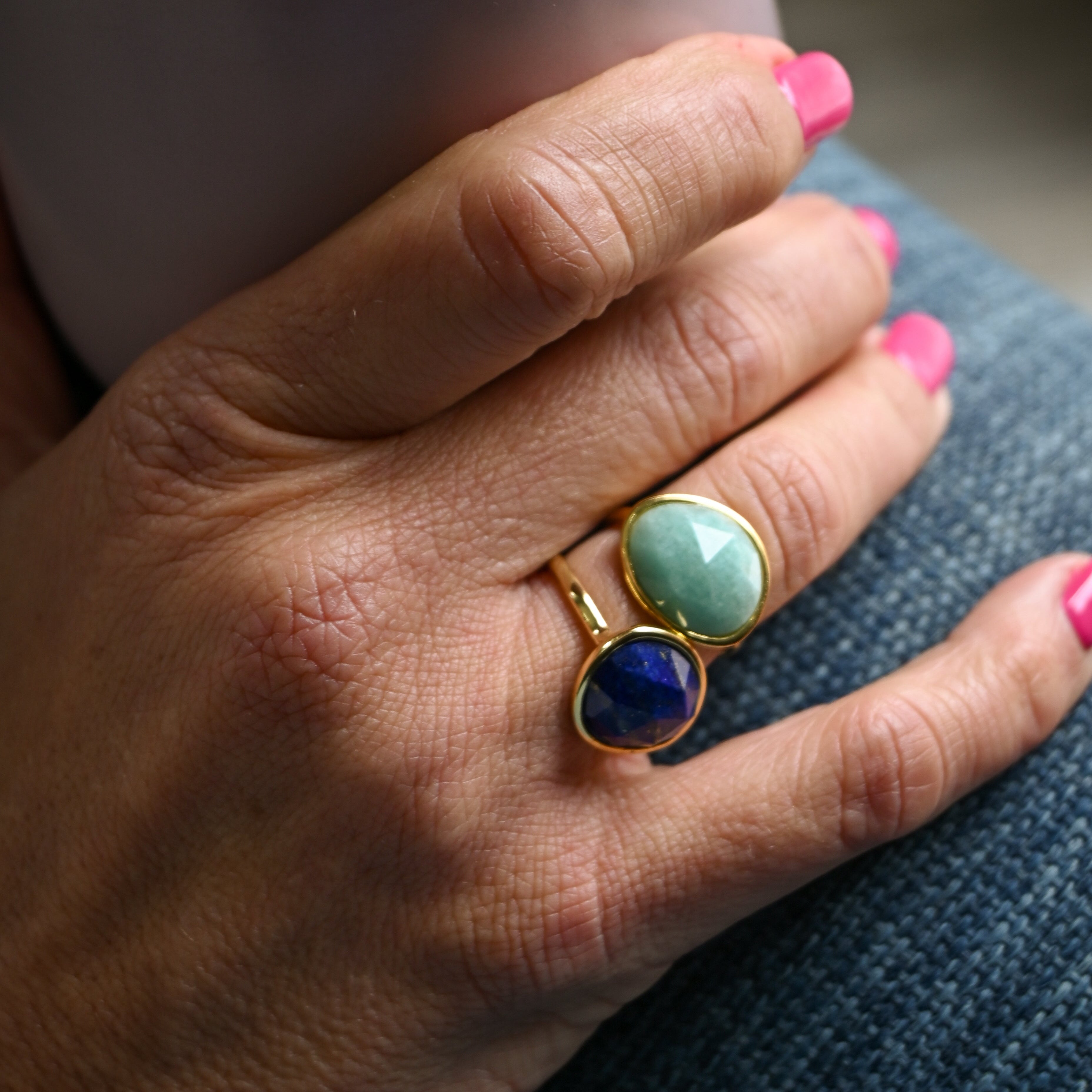 Hand wearing a gold ring with two colored stones, holding a pink mug.