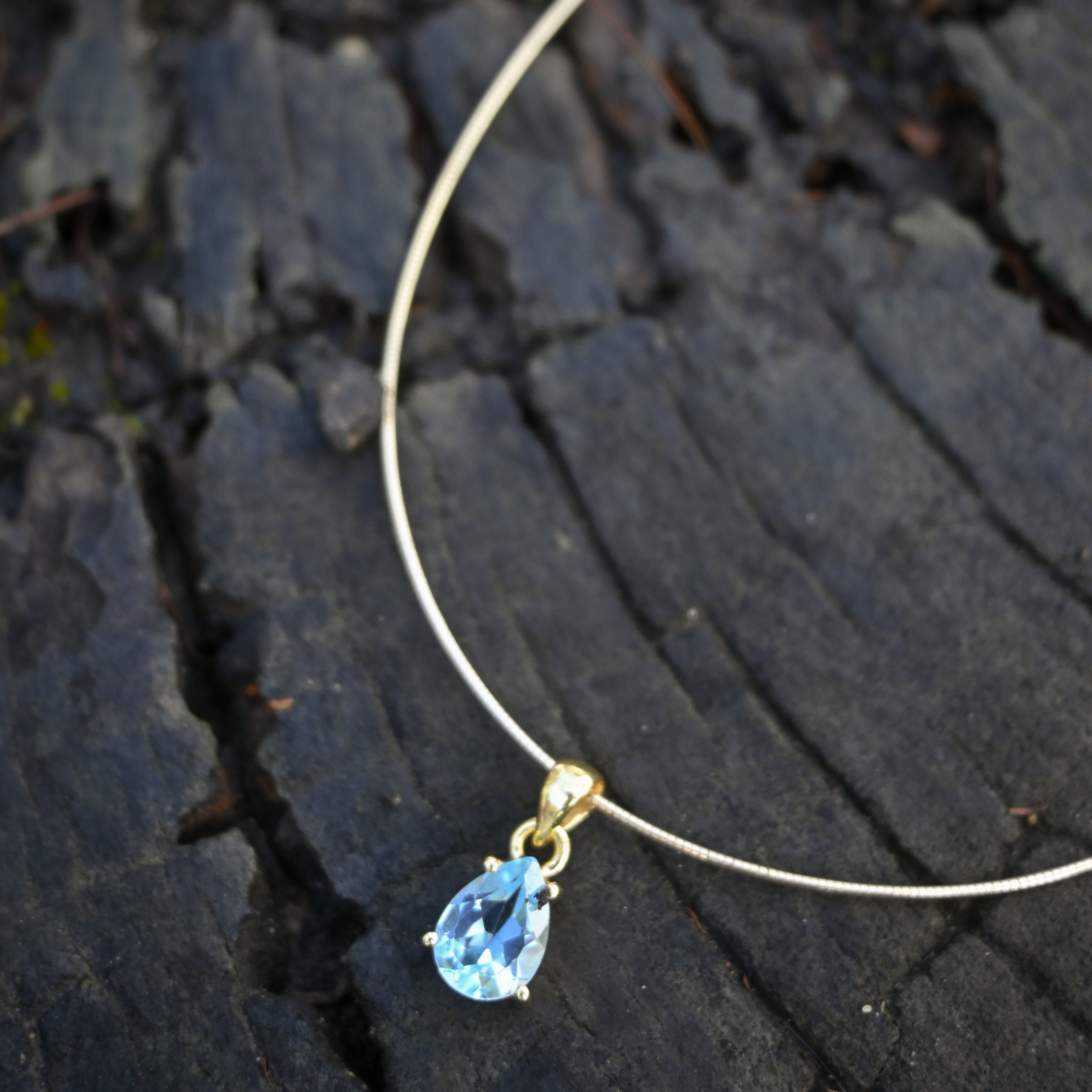 Necklace with a blue teardrop pendant on a dark textured surface