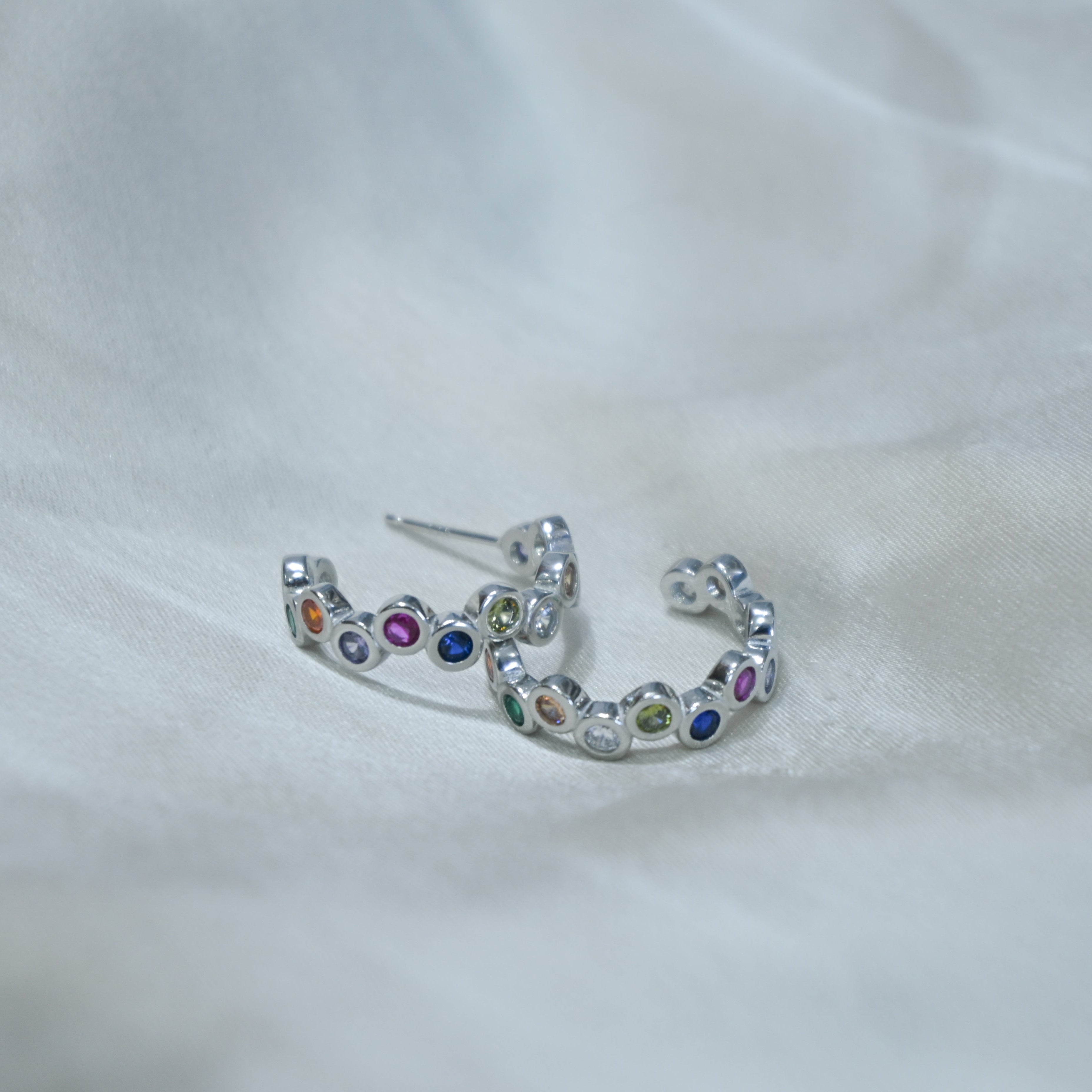 Silver earring with colorful gemstones on a white fabric background