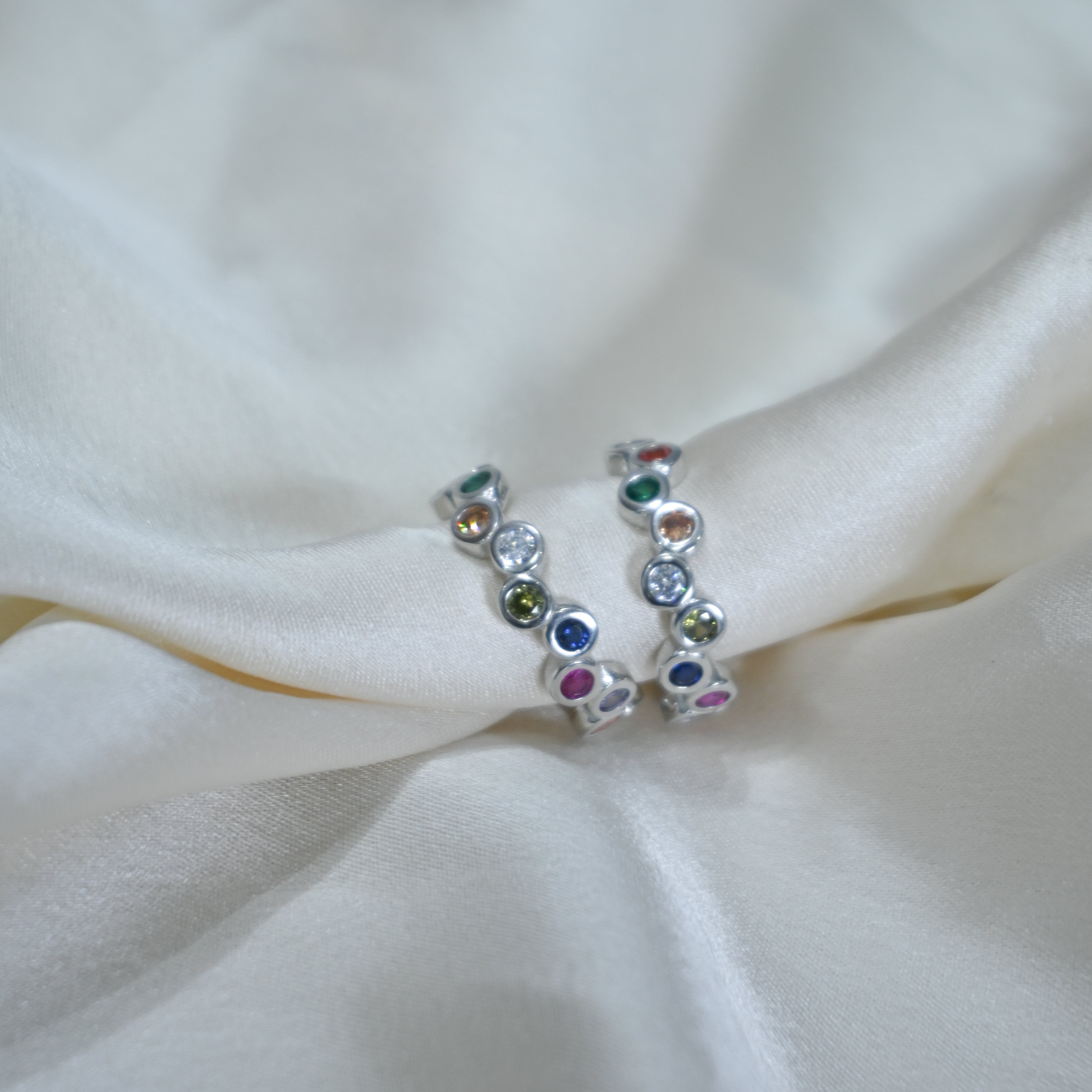 Silver ring with multicolored gemstones on a white fabric background