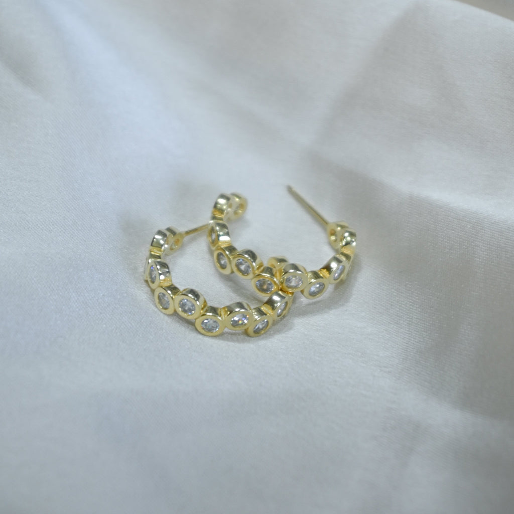 Gold hoop earrings with clear stones on a white fabric background
