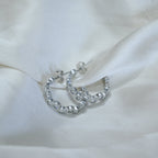 Silver hoop earrings with clear stones on a white fabric background