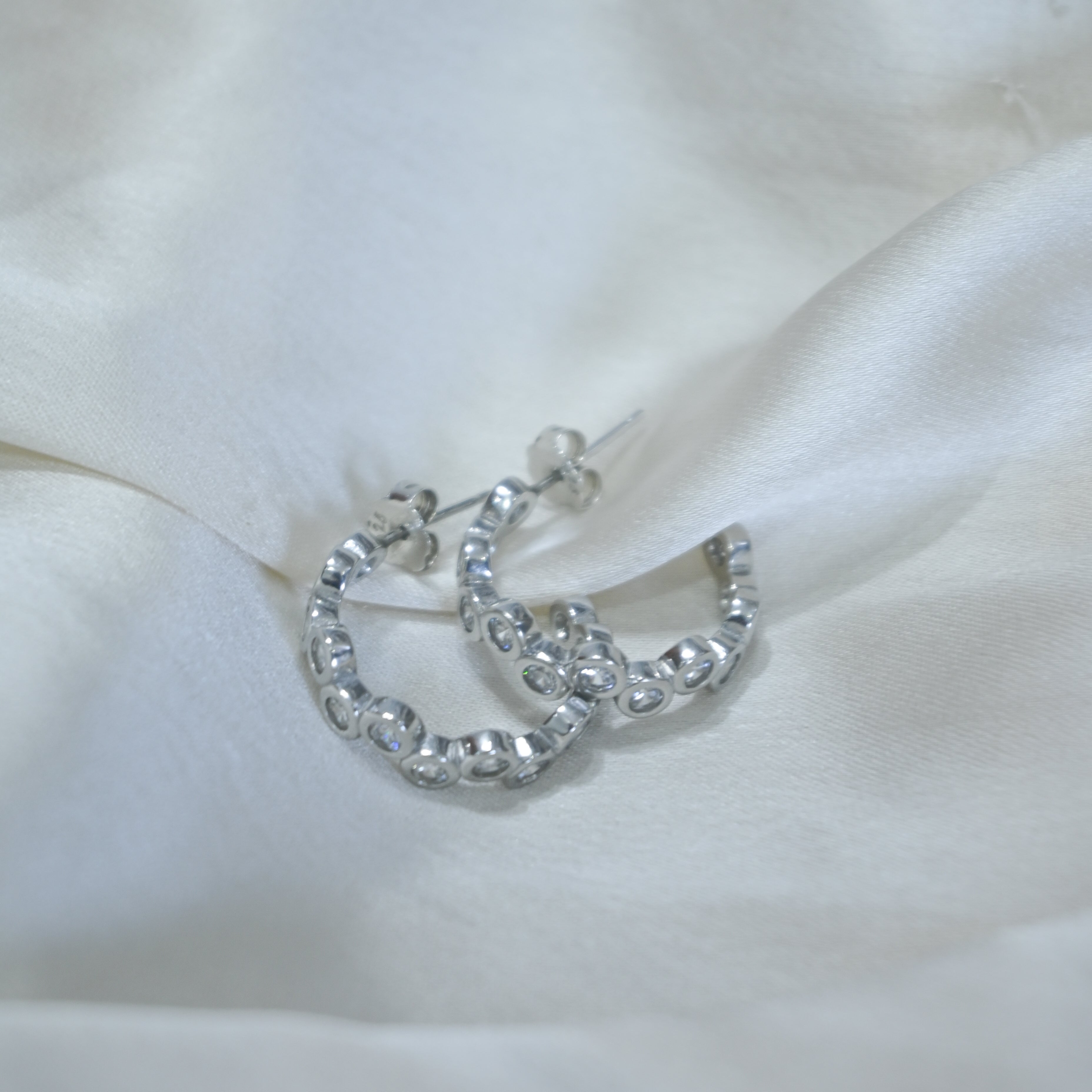 Silver hoop earrings with clear stones on a white fabric background