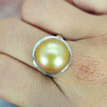 A gold/brown colored Mabe pearl ring set in a silver tube setting, displayed on a person's finger.