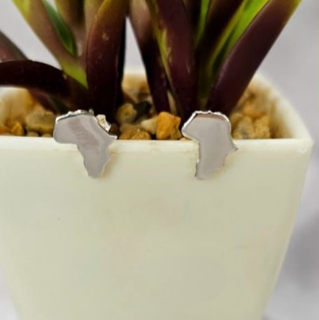 A pair of sterling silver studs in the shape of the African continent, displayed against a white vase with plants.