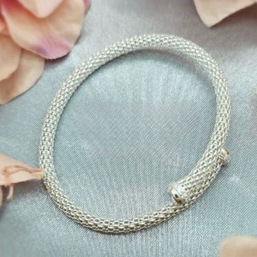 A sterling silver fold over mesh bangle bracelet displayed on a textured background with flower petals scattered around.