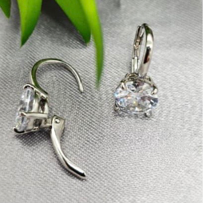 Silver earrings with clear gemstones on a gray surface with green leaves in the background