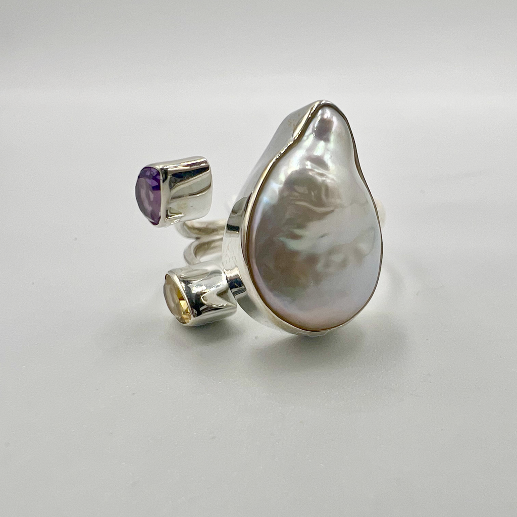 A sterling silver ring with a large pearl and two semi-precious stones, featuring an open band design.