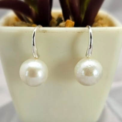 A pair of sterling silver drop earrings with large freshwater pearls, displayed in a white vase with a green plant.
