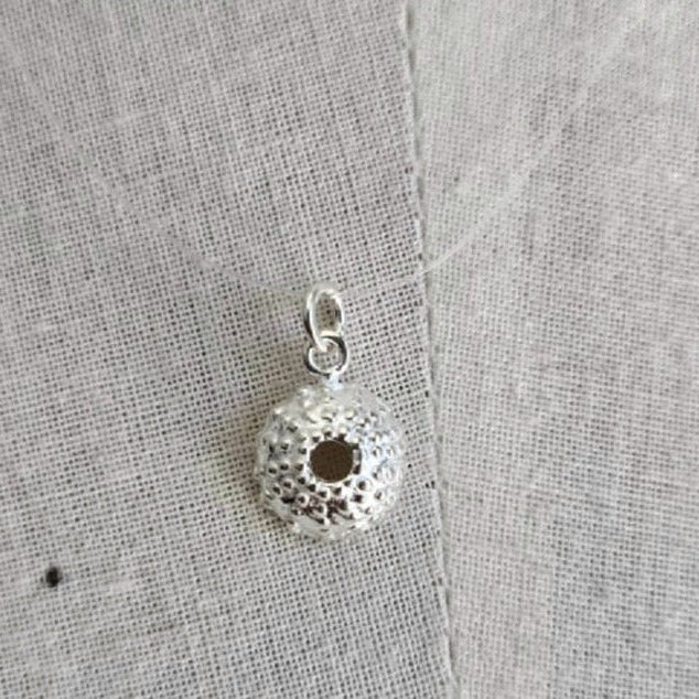 Silver pendant on a textured gray fabric background