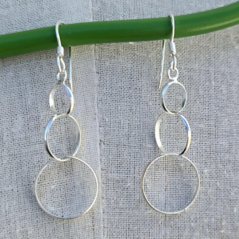 Silver circular earrings hanging on a green wire against a gray background
