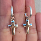 Silver cross earrings held on a hand against a neutral background