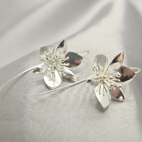 A pair of sterling silver floral earrings with a geometric pattern, displayed against a textured grey backdrop.