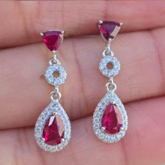 Teardrop-shaped red gemstone earrings with silver setting on a hand.