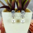 A pair of silver earrings featuring a floral design with cubic zirconia flowers and freshwater pearls, displayed on a plant pot.