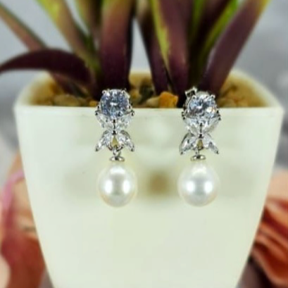 A pair of silver earrings featuring a floral design with cubic zirconia flowers and freshwater pearls, displayed on a plant pot.