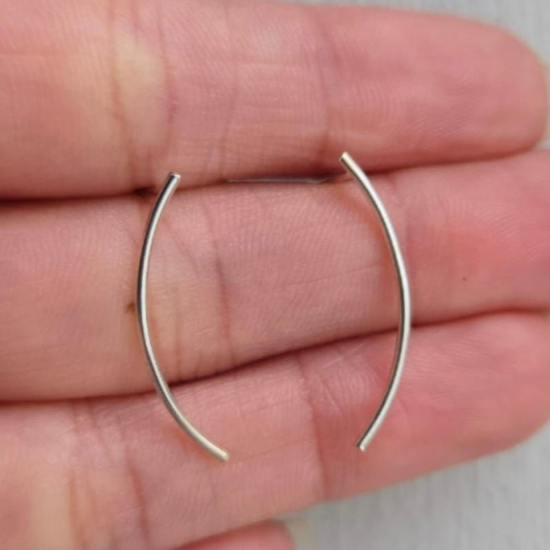 Silver hoop earrings held between two fingers on a neutral background