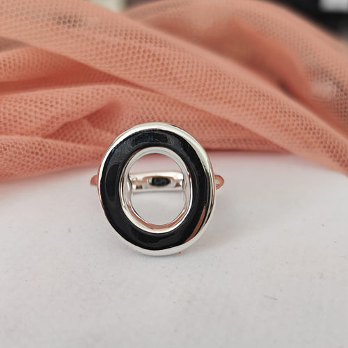 Silver ring with black center on a white surface with pink fabric in the background