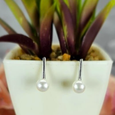 A pair of pearl hook earrings in white color displayed in a white pot with green leaves.