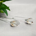 A pair of sterling silver tulip earrings with a geometric pattern, displayed on a textured grey background.