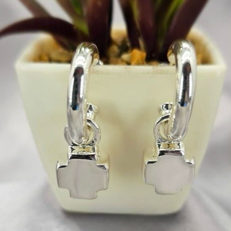 A pair of sterling silver cross-shaped earrings displayed in front of a potted plant.