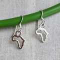 Silver horse-shaped earrings hanging on a green stick against a textured fabric background