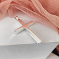 Silver cross pendant on a white surface with pink fabric in the background