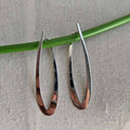 Silver hoop earrings on a green stick against a gray background