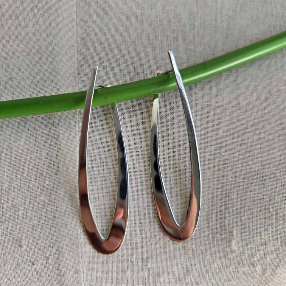 Silver hoop earrings on a green stick against a gray background