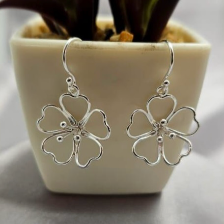 Sterling silver flower-shaped earrings displayed on a table with a potted plant in the background.