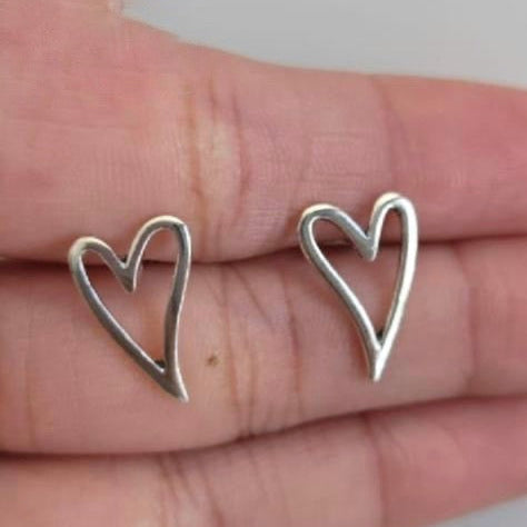 Silver heart-shaped earrings held between fingers against a neutral background