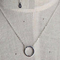 Silver necklace with a circular pendant on a gray fabric background