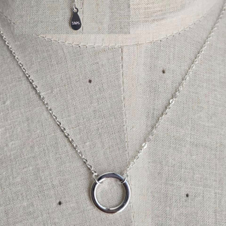 Silver necklace with a circular pendant on a gray fabric background