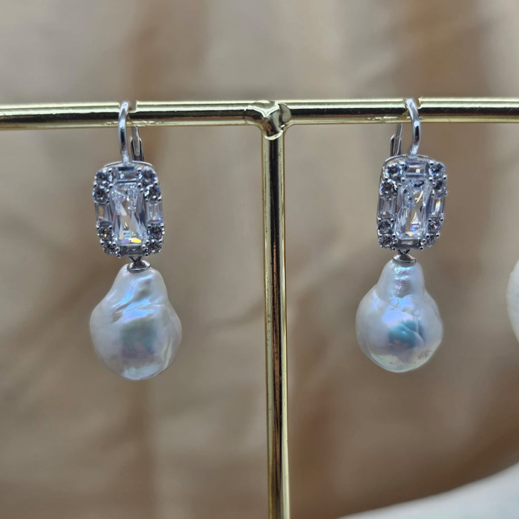 Pearl earrings with silver accents on a gold stand against a blurred background