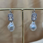 Pearl earrings with silver accents on a gold stand against a blurred background