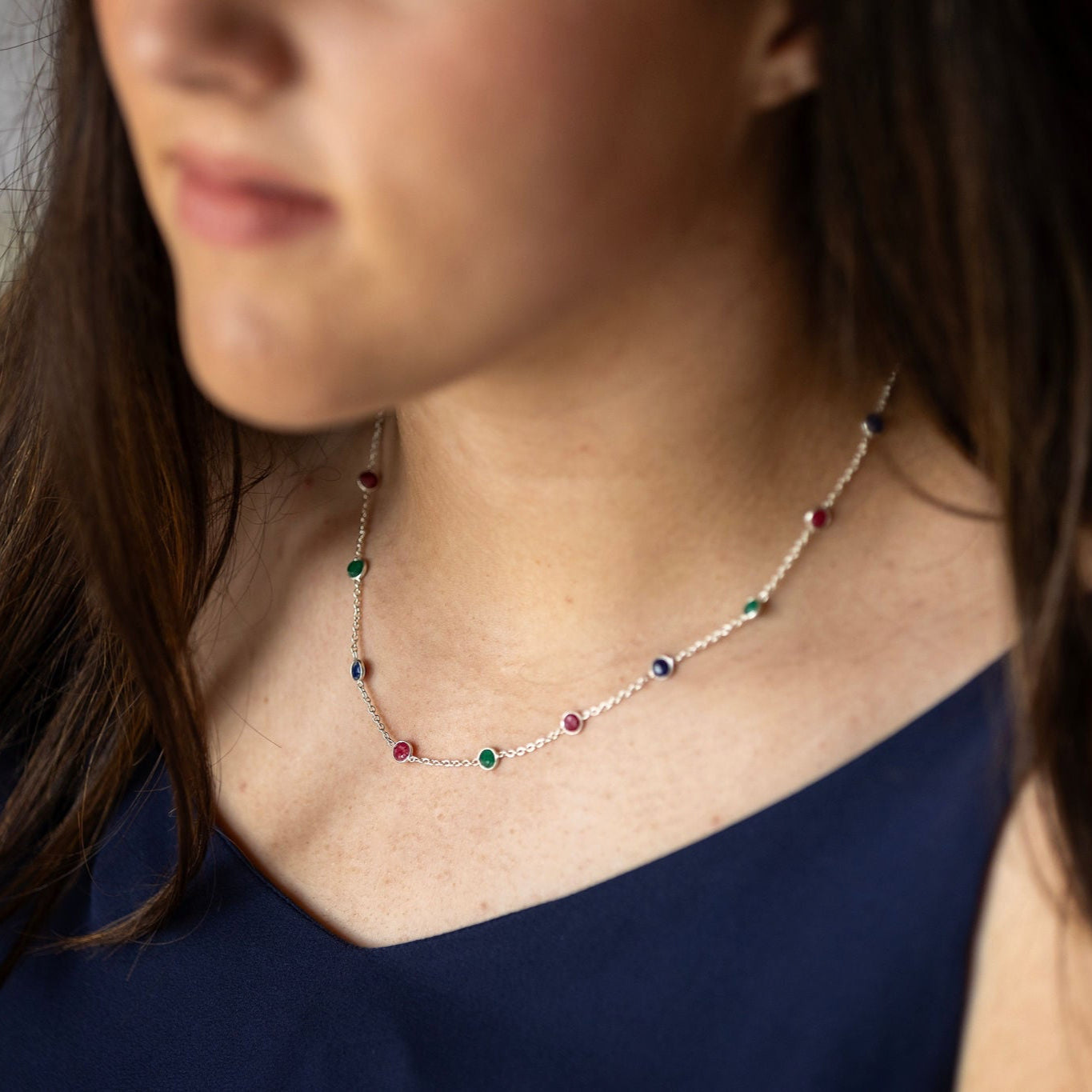 A person wearing a sterling silver necklace with blue, green, and red semi precious stones in a chain.