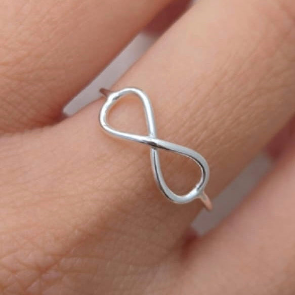 Silver infinity ring on a finger against a white background
